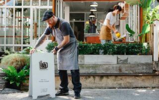 Hotel staff setting out a sign and tending to a garden to prepare for guests.