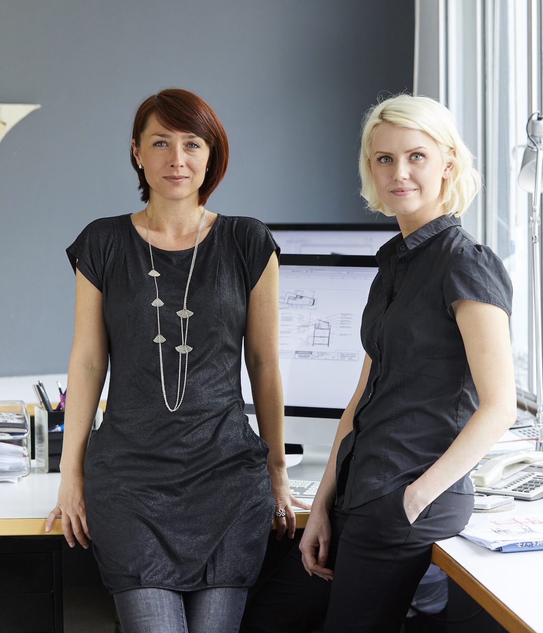 Portrait of two confident female designers at office desk Two colleagues in front of a computer in an office looking straight at the camera.