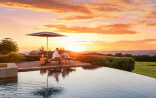 A couple relaxes by the pool at sunset while staying at a Spicers Retreats hotel.