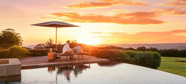 A couple relaxes by the pool at sunset while staying at a Spicers Retreats hotel.