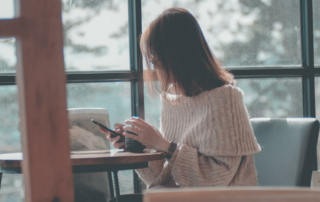A person sits at a table holding their phone while drinking coffee.