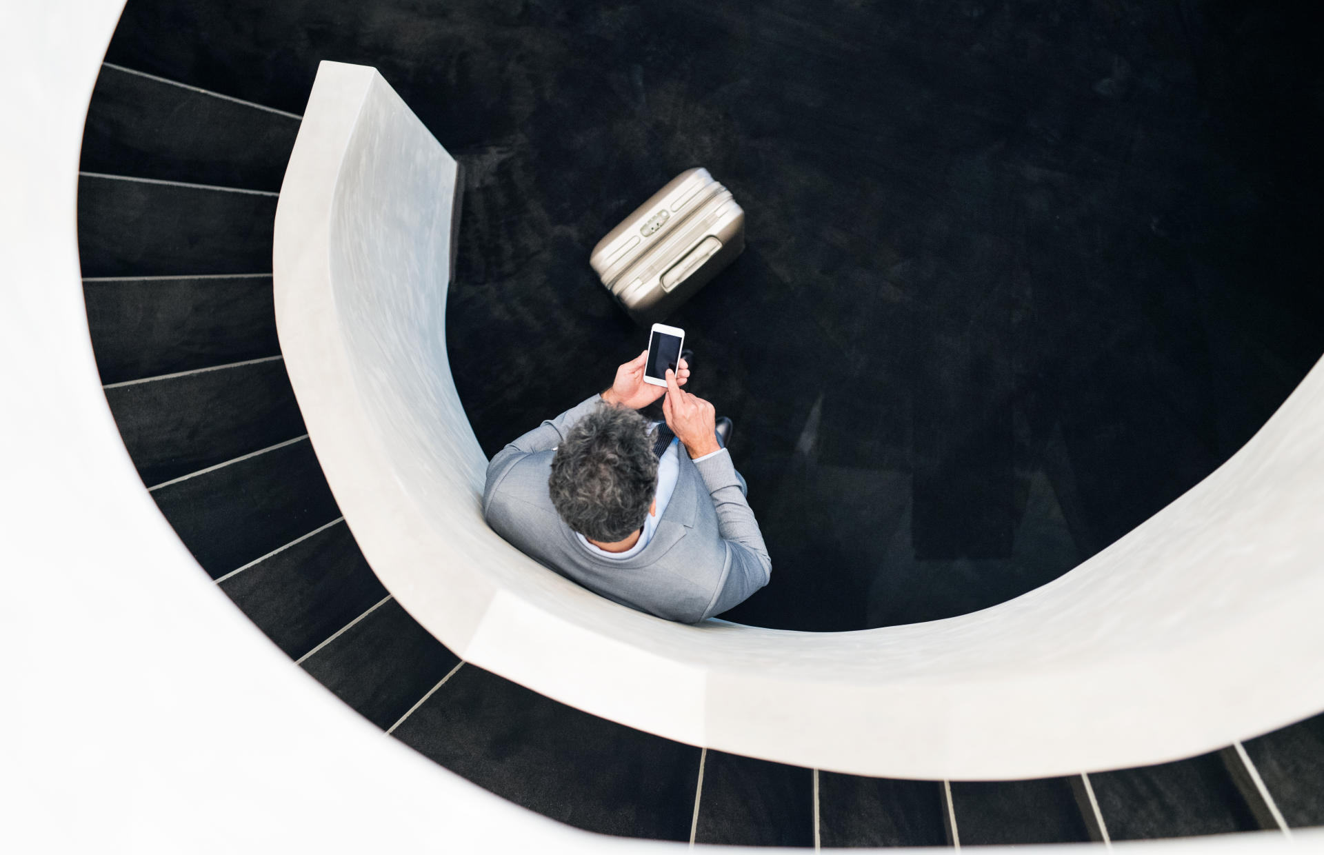 A business person waits by a staircase with their luggage.
