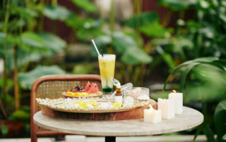 A cocktail sits on a small table with a side of fruit.