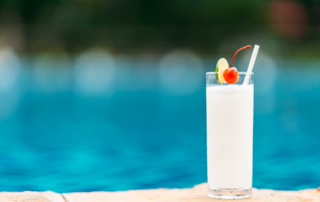 A coconut juice drink with a lime slice and a cherry sits at the edge of a pool.