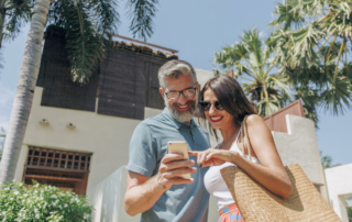 Two hotel guests look at a phone in front of a hotel.