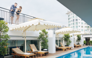 Two hotel guests stand on a balcony above a pool.