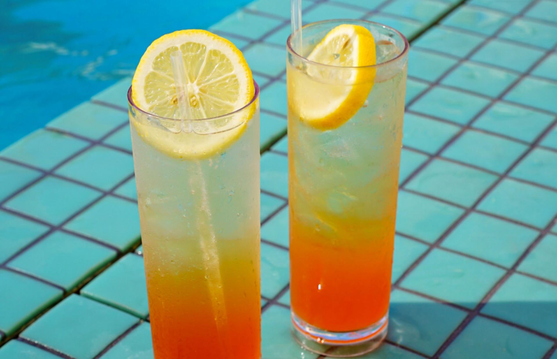 Two glasses with lemon slices sit by the pool.