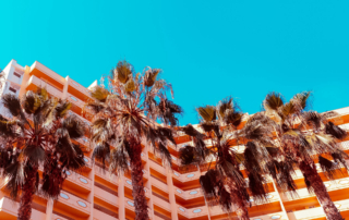 Palm trees stand in front of an orange hotel building.