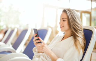 A hotel guest in a robe reclines on a chair and looks at their phone.