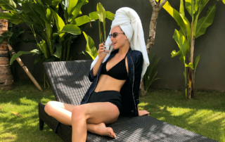 A hotel guest in a bathing suite reclines on a chair and has a beverage.