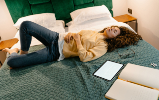 A hotel guest lays on the bed next to their mobile device.