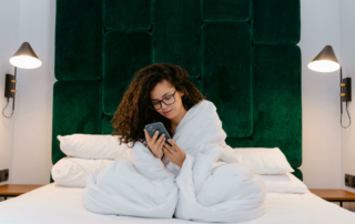 A guest wrapped in a comforter looks at their phone.