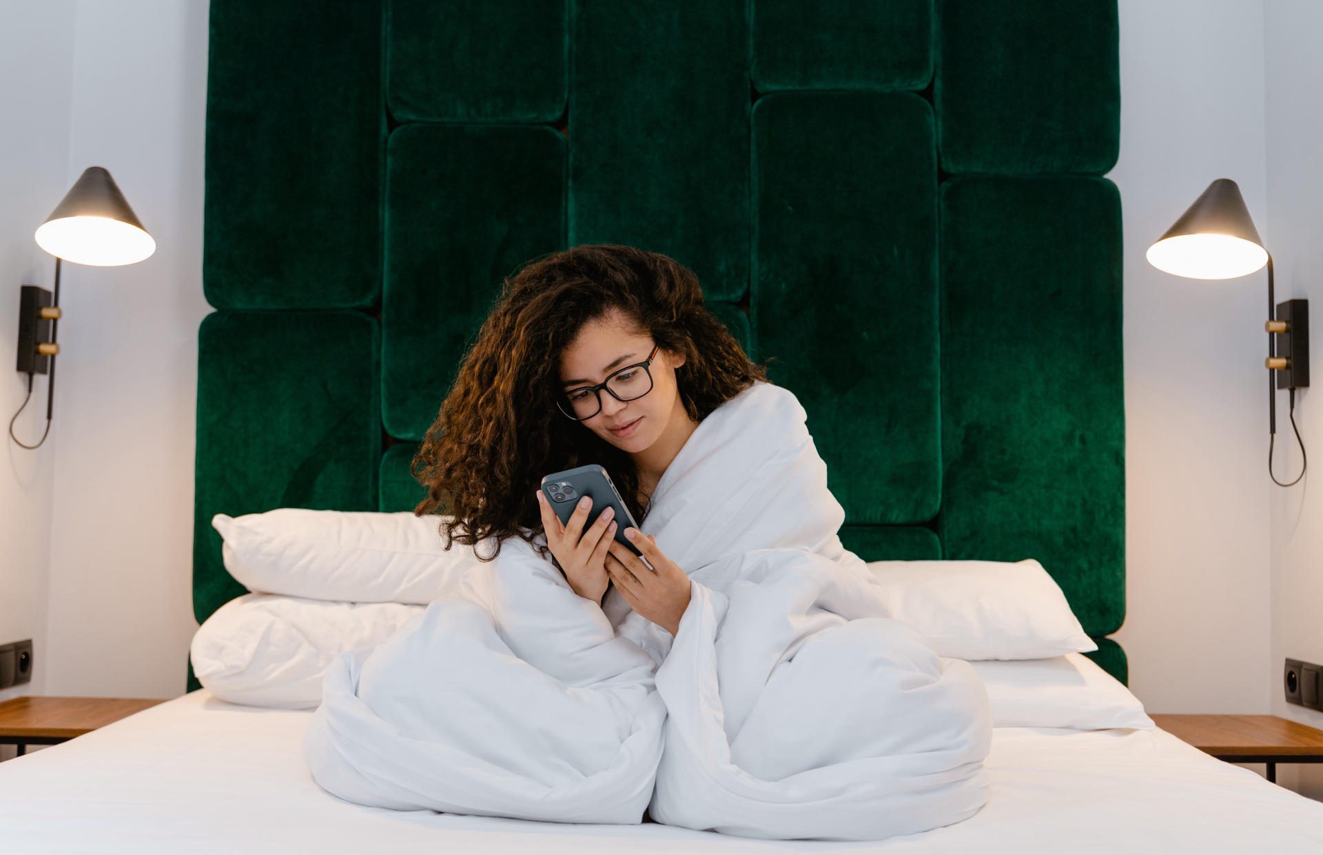 A guest wrapped in a comforter looks at their phone.