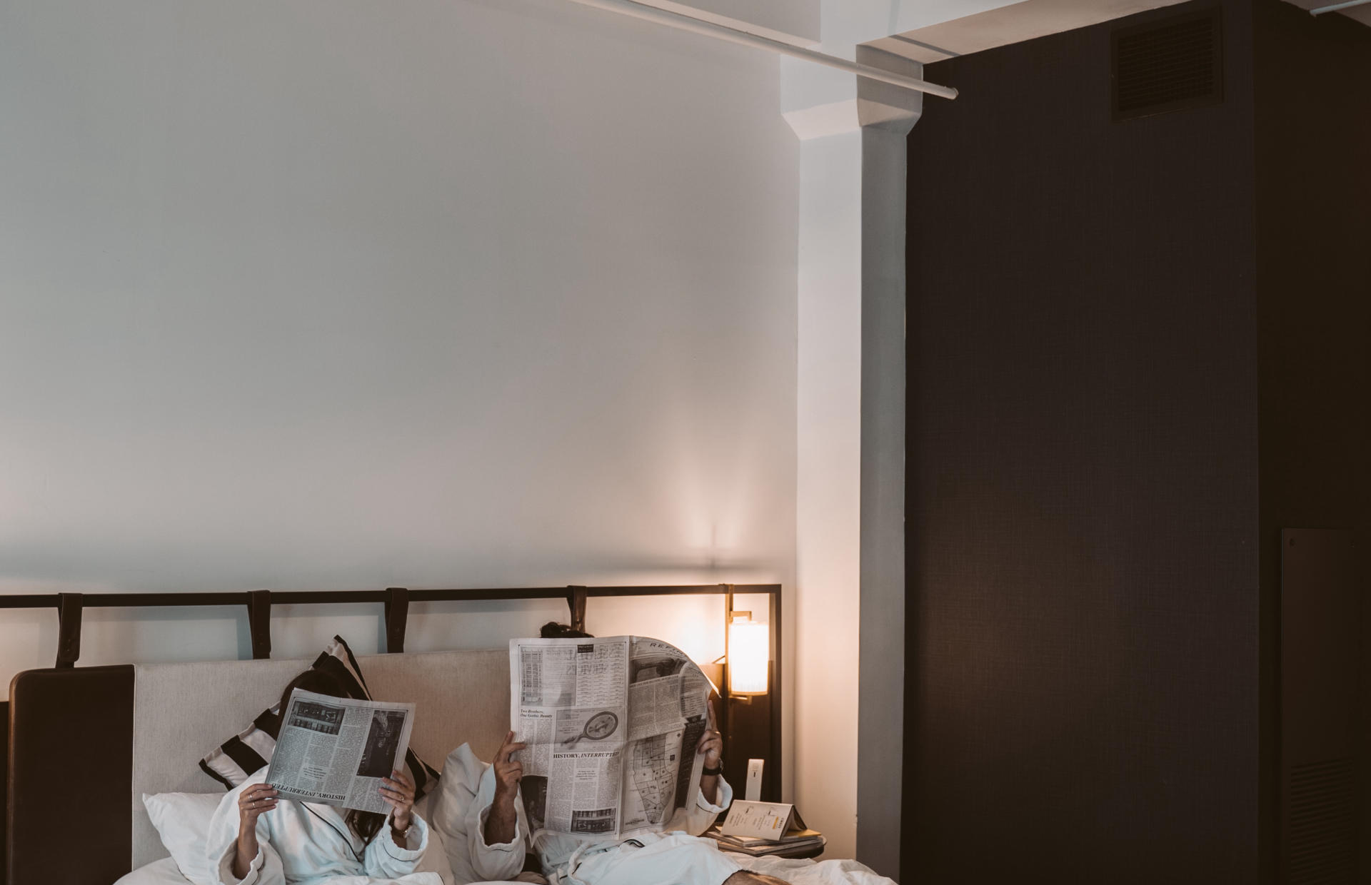 Two guests read the newspaper in bed.