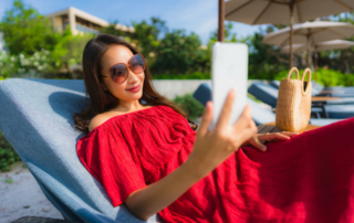 A woman reclining in a pool chair holds her phone in front of her face.