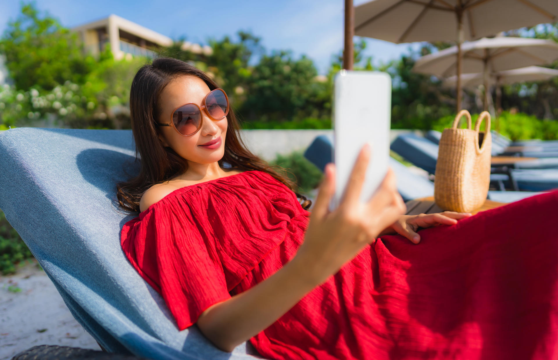 A woman reclining in a pool chair holds her phone in front of her face.