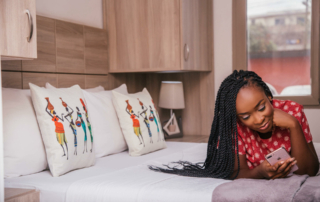 A woman is laying on her stomach on a hotel bed and looking at her phone.
