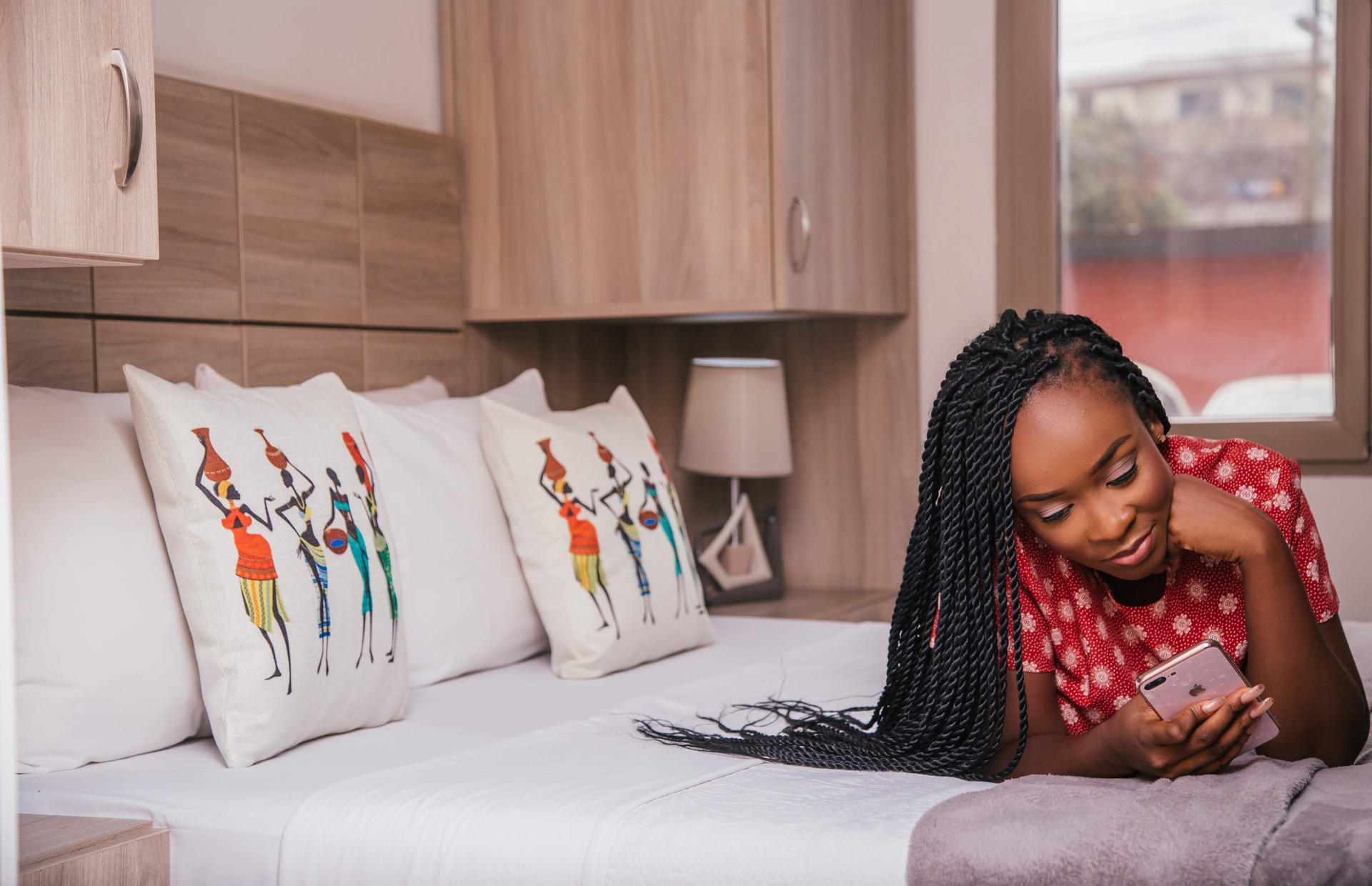 A woman is laying on her stomach on a hotel bed and looking at her phone.