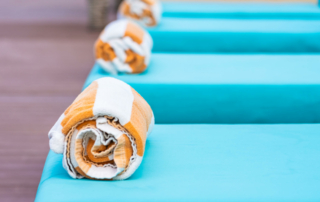 There are four blue pool chairs with striped rolled-up towels.