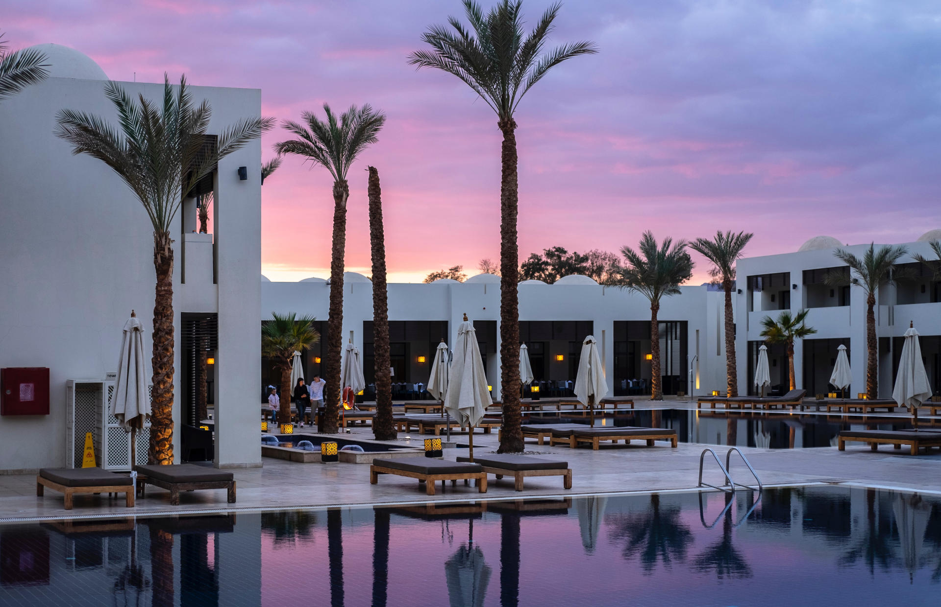 The pool area of a hotel is at sunrise or sunset.