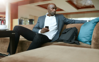 A business man is sitting on a couch in a hotel lobby with his phone in his hand.