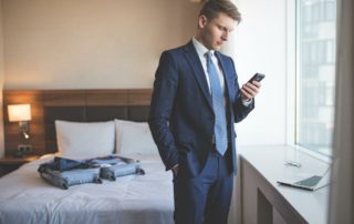A business man is in a hotel room standing in front of a window while looking at this phone.