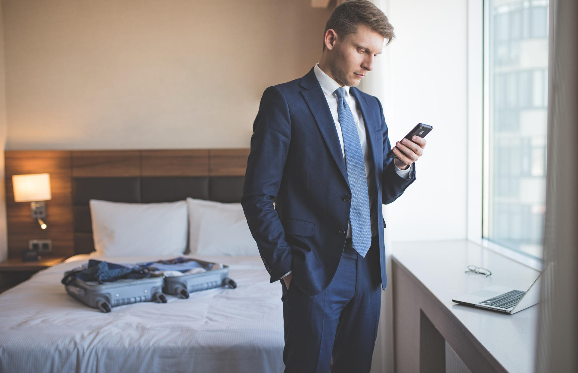 A business man is in a hotel room standing in front of a window while looking at this phone.