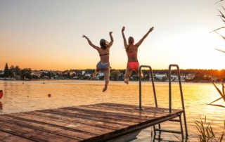 2 women jump into a lake at sunset