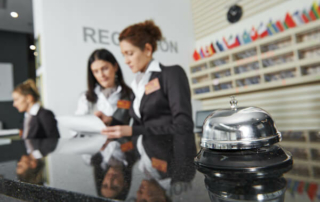 Two women discuss at a hotel front desk with a bell.