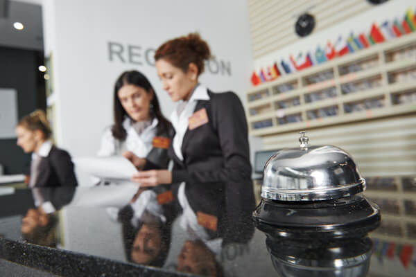 Two women discuss at a hotel front desk with a bell.