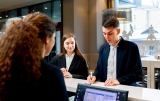 Female hotel receptionist checks in male and female guests.