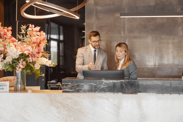 A male and female hotelier review data on a computer
